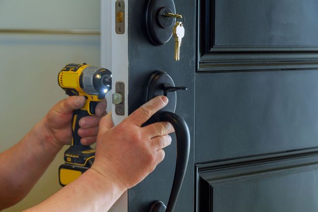 Hands installing a black door handle with a power drill